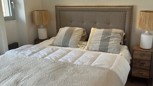 A neatly made bed with a striped pillow, two bedside lamps, and a wall-mounted light fixture. - Magnificent renovated air-conditioned rooftop terrace/50m from the sea. (CAVALAIRE SUR MER)