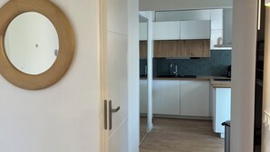 A hallway leading to a kitchen with white cabinets, a wooden floor, and a round mirror on the left. - Magnificent renovated air-conditioned rooftop terrace/50m from the sea. (CAVALAIRE SUR MER)