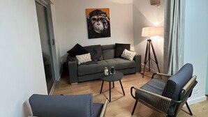 A modern living room with a grey sofa, two wicker chairs, a coffee table, and a painting on the wall. - Magnificent renovated air-conditioned rooftop terrace/50m from the sea. (CAVALAIRE SUR MER)