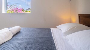 Ett sovrum med en säng, ett fönster med utsikt över blommor och ett hus samt en luftkonditioneringsanläggning.