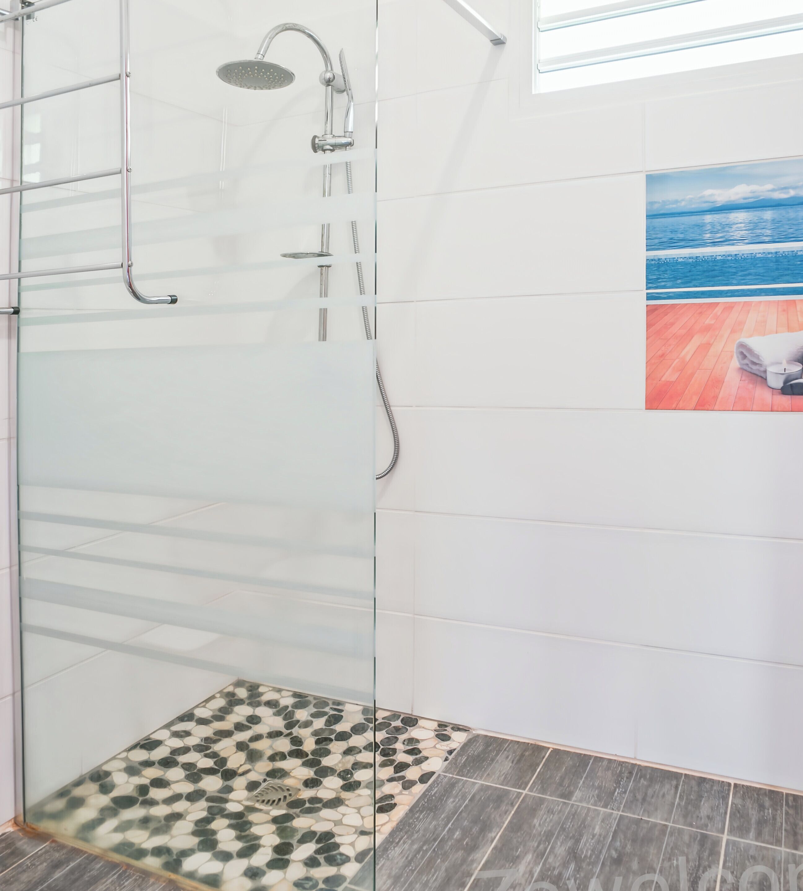 A glass-enclosed shower with a rain showerhead, a glass door, and a tiled floor with a pebble pattern.