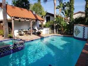 A swimming pool with tiled edges, a covered patio with outdoor furniture, and surrounding greenery.