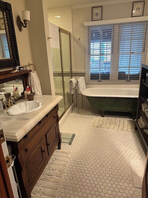 A bathroom with a white sink, wooden vanity, a glass shower enclosure, a green bathtub, and a window with blinds.
