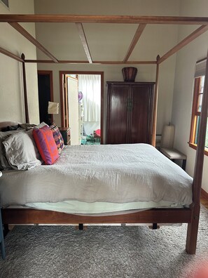 Una cama con dosel de madera, un banco, un armario y un ventanal con cortinas.