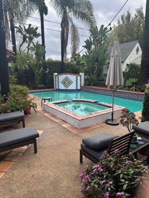 Piscina con solárium de baldosas, rodeada de sillones de descanso y plantas en macetas.