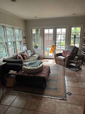 A living room with a sofa, ottoman, and a chair. There is a rug, a lamp, and a bookshelf.