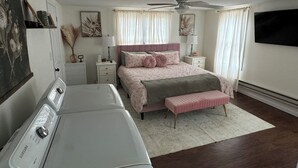 Un dormitorio con cama, mesitas de noche, ventilador de techo, televisión y lavadora.