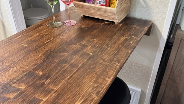 Una mesa de comedor de madera con dos copas de vino y una cesta que contiene una botella de champán, bocadillos y una botella de Welch's.