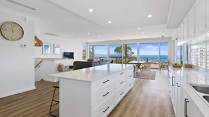A modern kitchen with a large island, white cabinetry, and a view of the ocean. - Norman Views - 20 Panorama Crescent (Normanville)