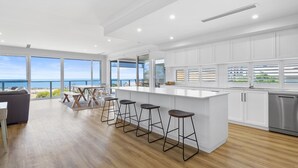 A modern kitchen with a large island, bar stools, and a view of the ocean. - Norman Views - 20 Panorama Crescent (Normanville)