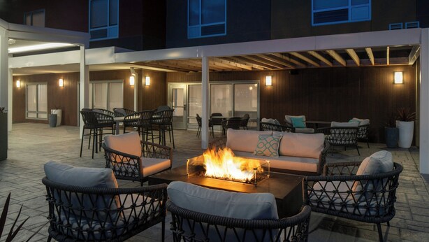 An outdoor patio area with wicker furniture, a fire pit, and a view of a building in the background. - TownePlace Suites by Marriott West Lafayette (West Lafayette)