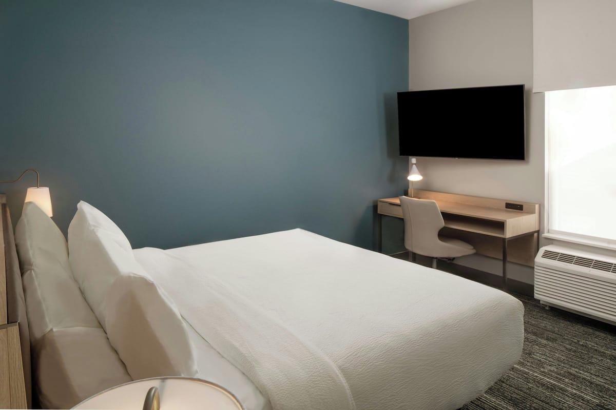 Ein Hotelzimmer mit Bett, Schreibtisch, Stuhl, Fernseher und Fenster.