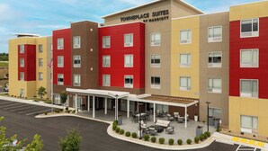 A multi-story hotel with a modern design, featuring a mix of red, yellow, and beige colors. The hotel has a covered outdoor area with seating and a flagpole with an American flag. - TownePlace Suites by Marriott West Lafayette (West Lafayette)