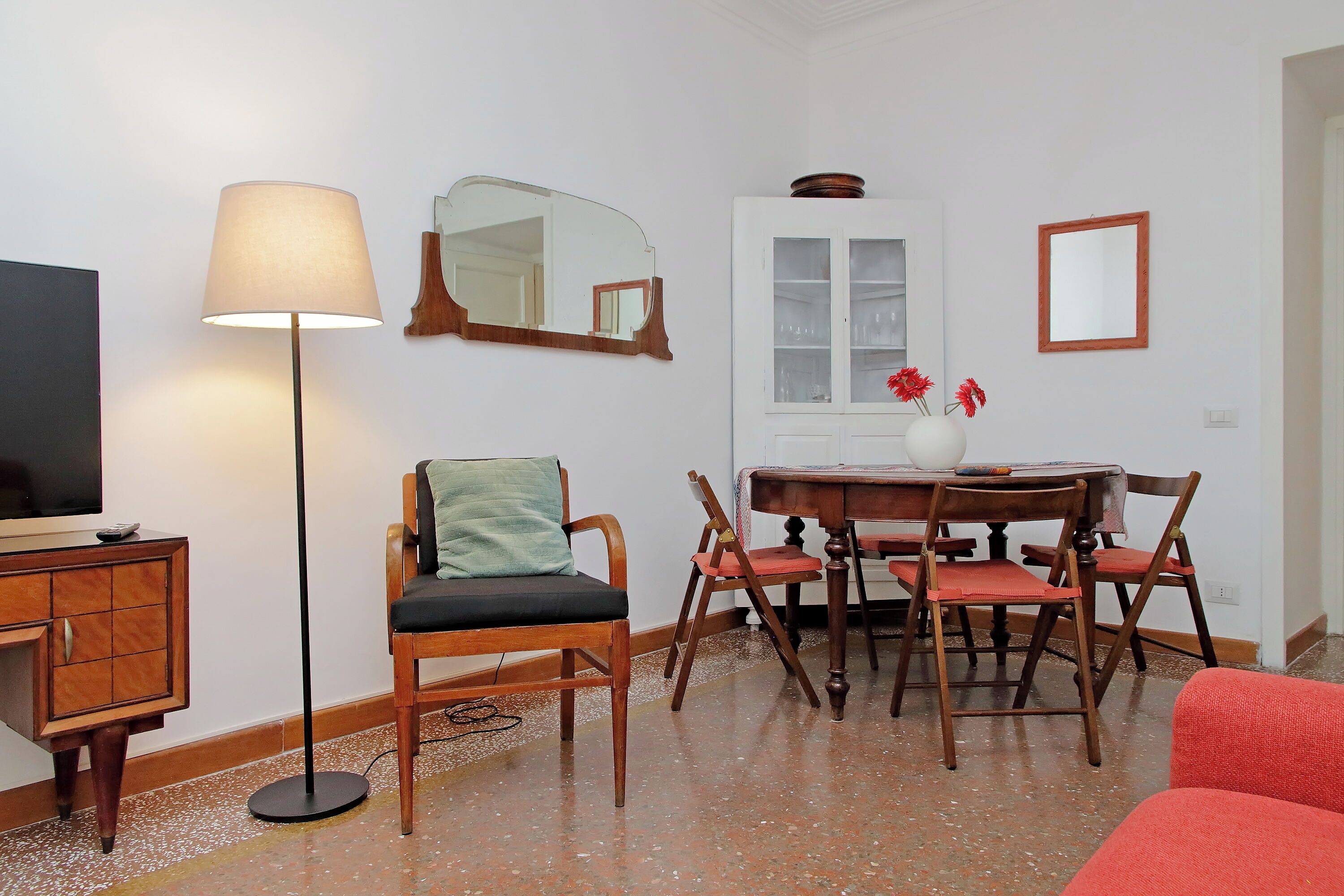 A living room with a TV, a lamp, a dining table with chairs, and a cabinet.