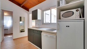 Una cocina compacta con techo de madera, armarios blancos, lavavajillas y microondas.