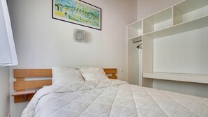 Un dormitorio con una cama, cabecera de madera, ropa de cama blanca, un estante montado en la pared y un cuadro enmarcado.