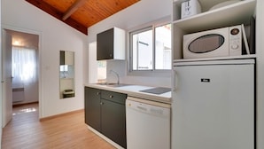 A compact kitchen with a wooden ceiling, white cabinets, a dishwasher, and a microwave. - Gite 2 bedrooms 5 persons (L'AIGUILLON-LA-PRESQU'ÎLE)
