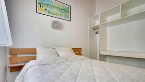 A bedroom with a bed, wooden headboard, white bedding, a wall-mounted shelf, and a framed picture. - Gite 2 bedrooms 5 persons (L'AIGUILLON-LA-PRESQU'ÎLE)
