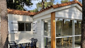 A small, white building with a tiled roof, a table with chairs, and a large glass door. - Gite 2 bedrooms 5 persons (L'AIGUILLON-LA-PRESQU'ÎLE)