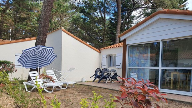 A patio with white lounge chairs, a striped umbrella, and a small garden area with plants. - Gite 2 bedrooms 5 persons (L'AIGUILLON-LA-PRESQU'ÎLE)