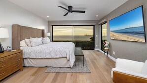 Un dormitorio moderno con una cama grande, un ventilador de techo, vista al océano y un cuadro de playa.