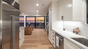 Una cocina moderna con una isla grande, horno empotrado y vistas al atardecer a través de amplias ventanas.