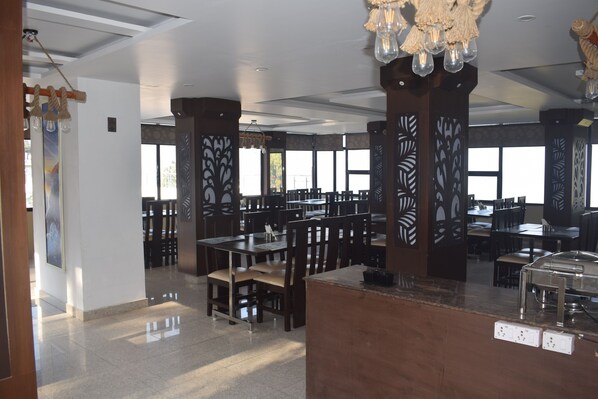 A spacious restaurant with high ceilings, large windows, and modern decor. - Hotel Kavita Palace (Lansdowne)