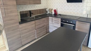 A modern kitchen with wooden cabinets, a black countertop, a built-in oven, and a wall-mounted TV. - Superb sea view apartment with private pool! 5 minutes from the center of Roses. (Roses)