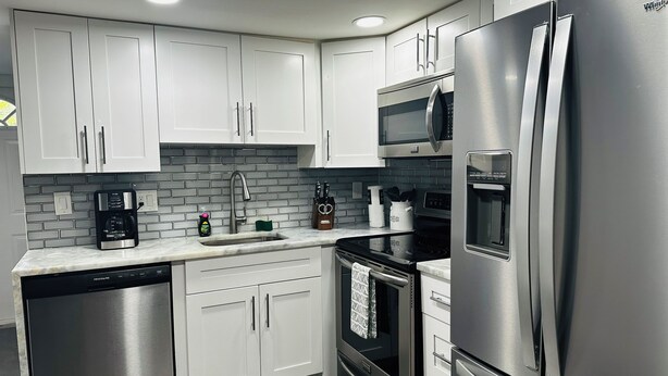 Una cocina moderna con electrodomésticos de acero inoxidable, armarios blancos y un salpicadero de azulejos.