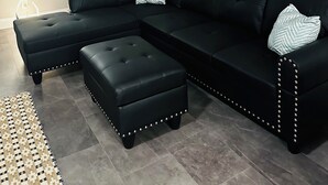 Una sala moderna con un sofá seccional negro, un reposapiés a juego y un cuadro grande de una puesta de sol sobre el océano.