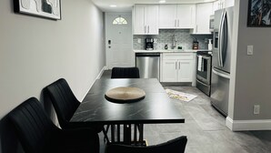 Una cocina moderna con armarios blancos, electrodomésticos de acero inoxidable y una mesa de comedor de mármol.