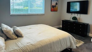 Un dormitorio con cama, cómoda, televisor y ventana con persianas.