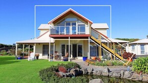 Une maison à deux étages avec un balcon, un porche à l’avant et un petit jardin agrémenté d’un bassin.