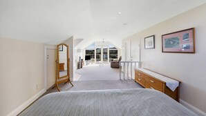 Une chambre avec un grand lit, une commode, une coiffeuse et un miroir. Une porte donne sur un balcon d’où l’on peut admirer le paysage.