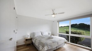 Een slaapkamer met een groot raam, een plafondventilator en een net opgemaakt bed.