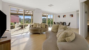 A spacious living room with a large sofa, a smaller armchair, and a dining area with chairs. There is a sliding glass door leading to an outdoor patio.