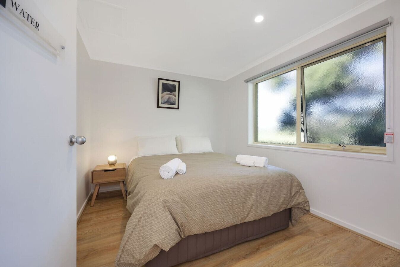 A bedroom with a bed, a nightstand, a window, and a door labeled "WATER".