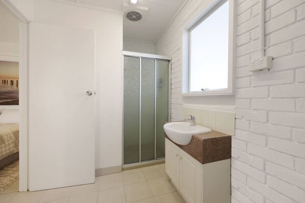 A bathroom with a shower, a sink, and a window.