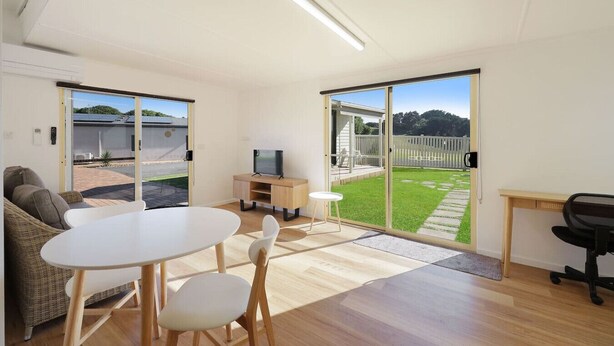 A modern living room with a dining table, a sofa, a TV, and a sliding glass door leading to a backyard. - Logans Beach Apartments - Lil Greenviews (Warrnambool)