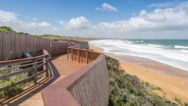 Une promenade en bois qui mène à une plage offrant une vue dégagée sur l’océan.
