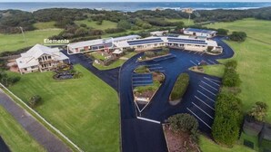 Un grand bâtiment doté d’une allée incurvée et d’un parking, entouré de verdure et offrant une vue sur l’océan.
