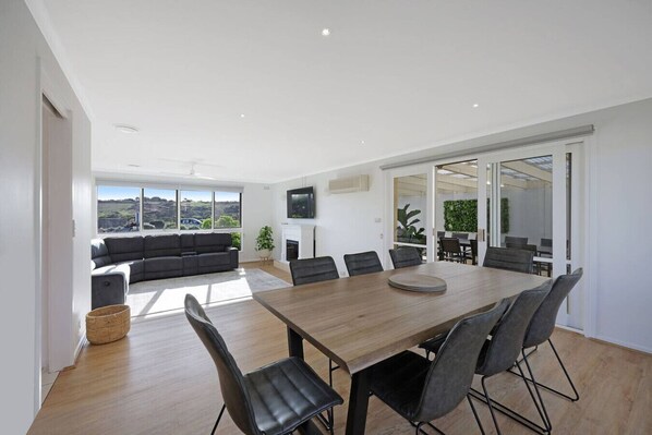 A modern living room with a large sofa, a dining table with chairs, and a fireplace.