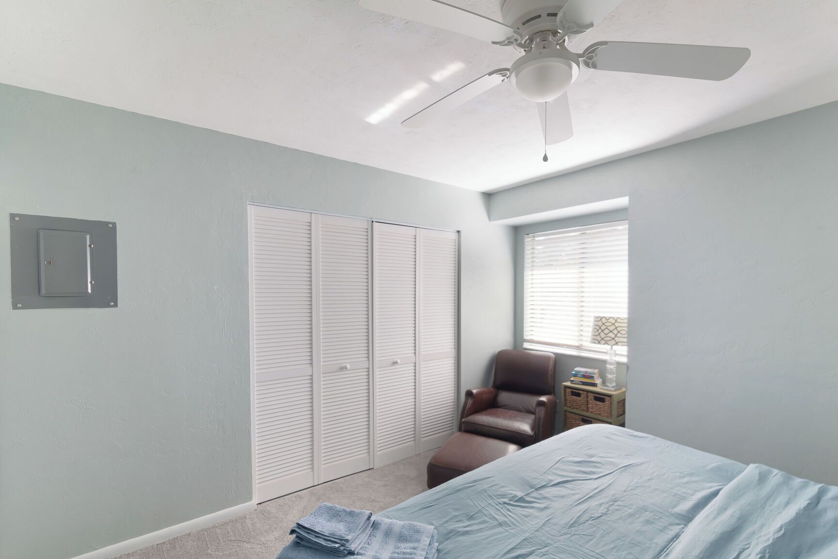 Une chambre à coucher avec un lit, une chaise, une armoire et un ventilateur de plafond.