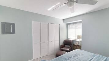 Une chambre à coucher avec un lit, une chaise, une armoire et un ventilateur de plafond.