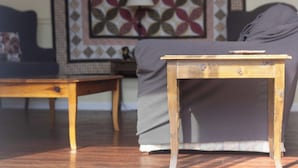 Ein Holztisch und ein Beistelltisch in einem Wohnzimmer mit einem gemusterten Wandbild und einer Couch.
