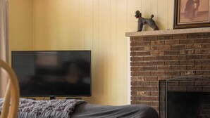 Ein Wohnzimmer mit Flachbildfernseher, Kamin aus Ziegelsteinen und einem gerahmten Bild von einem Hund.