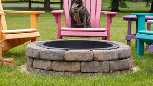 Ein Hund sitzt auf einem rosafarbenen Adirondack-Sessel vor einem Kamin aus Stein.
