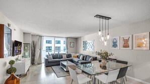 A modern living room with a sofa, a glass dining table, and a TV mounted on the wall.