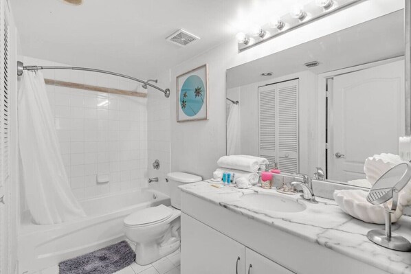 A bathroom with a bathtub, toilet, vanity with a mirror, and a shower curtain.