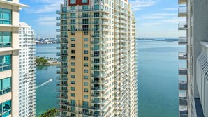 A high-rise hotel with multiple balconies, a view of the water, and a cityscape in the background.